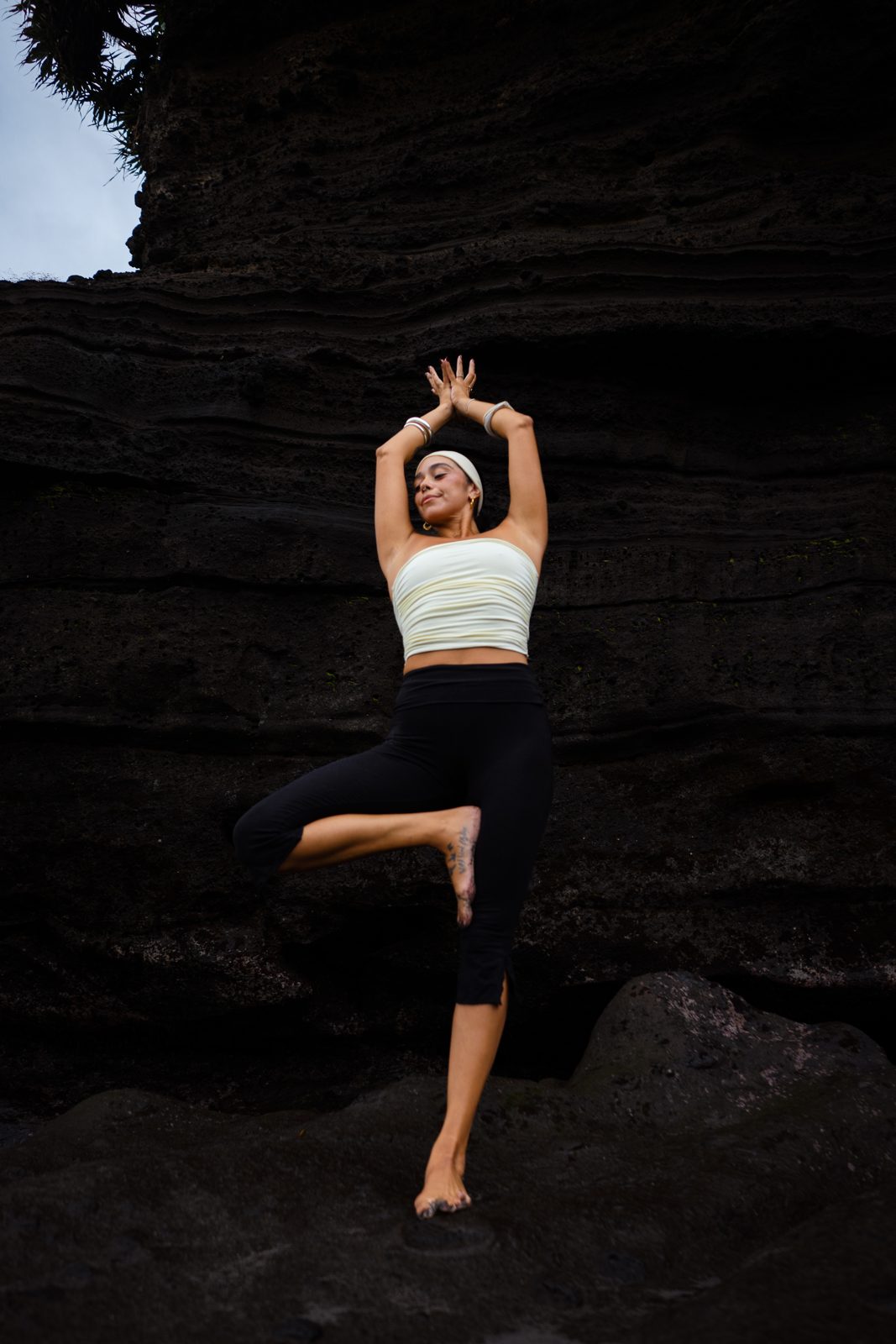 Irene del Valle in tree pose against a black volcanic rock face
